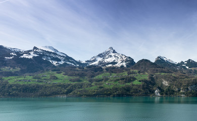 beautiful turquoise mountain lake panorama with snow-covered peaks and green meadows and forests