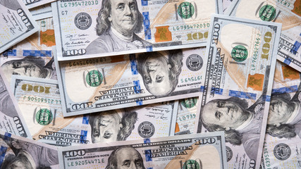 Pile of one hundred dollar denomination dollar banknotes spread unevenly.