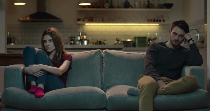 Couple sit apart on a sofa after an argument.
