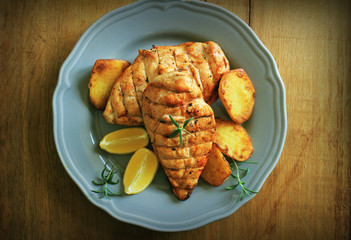 Grilled chicken breast with fried potato and lemon. Top view