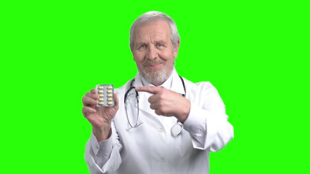 Senior doctor recommend pack of pills. Portrait of doctor with thumb up. Green screen hromakey background for keying.