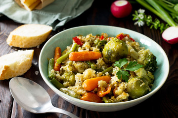 Healthy proper nutrition. Homemade vegetarian couscous with string beans, brussels sprouts, carrots, sweet peppers and tomatoes on a dark rustic wooden kitchen table.