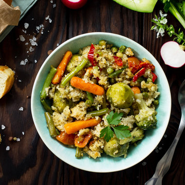 Healthy dietary vegan dish: couscous and vegetables (string beans, brussels sprouts, carrots, sweet peppers, tomatoes) on a dark rustic wooden kitchen table. Top view flat lay background.