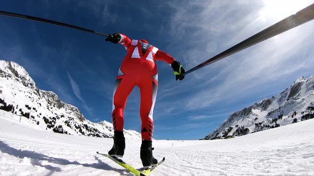 back view male cross country skier in race suit skating on cross country ski trail  on sunny winter day low perspective in slow motion
