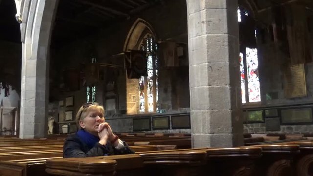 An old lady praying in a church whilst being sat down, Newcastle upon Tyne, United Kingdom 