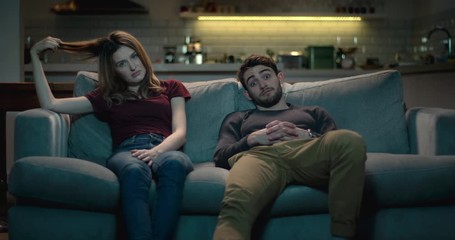 Extremely bored and frustrated couple sitting on a sofa at home struggle to watch a terrible movie.. - Powered by Adobe