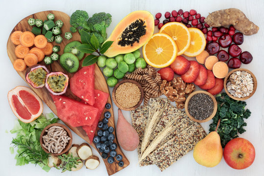 High fibre health food concept with multi seed crackers, cereals, nuts, fruit, vegetables and herbs. Foods high in omega 3 fatty acids, antioxidants, anthocynins and vitamins. Rustic background.