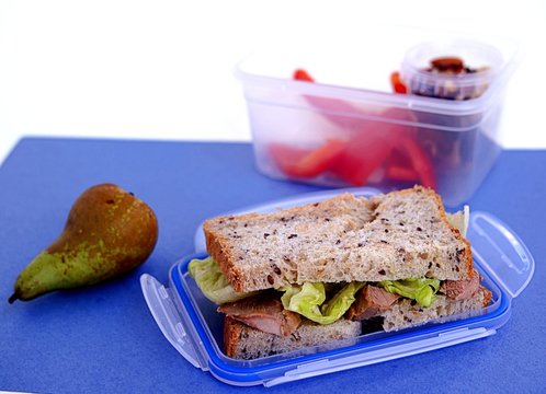 The concept of school food. Lunch box for the student. Sandwich of corn bread with baked turkey and crispy lettuce leaves, pear, nut mix, sweet pepper