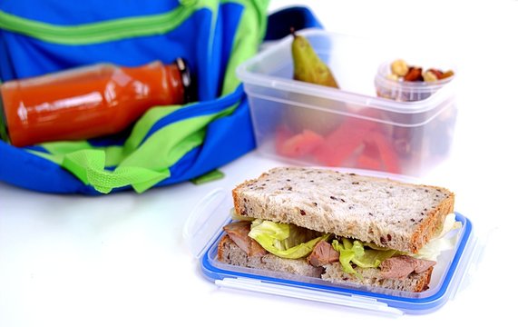 The concept of school food. Lunch box for the student. Sandwich of corn bread with baked turkey and crispy lettuce leaves, pear, nut mix, sweet pepper, carrot juice