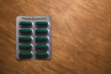 Green pills in blister pack on the wooden surface