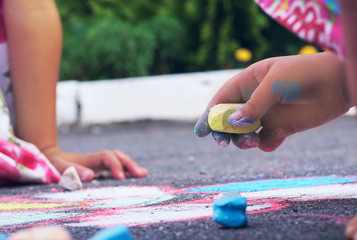 Yellow chalk in the hands of a girl drawing on the asphalt. The child drawing a chalk on asphalt.