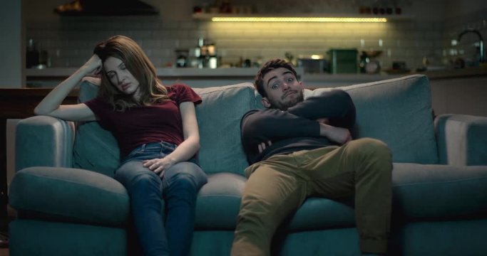Frustrating relationship - couple at home sitting on a sofa struggling with each others company.