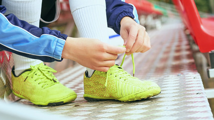 Boy football soccer tying the laces on the boots on grassy football stadium.