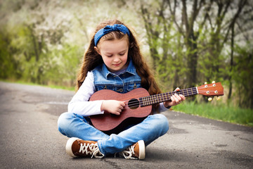 Pretty young girl playing ukulele in the park