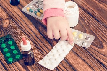 Children's hands with medicines on a wooden table. A small child left unattended plays dangerous...