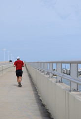 Fit man jogging up concrete bridge, blue sky.