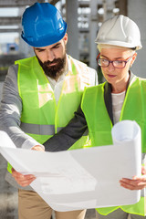 Young female and male engineers or business partners at construction site, working together on building's blueprint. Architecture and teamwork concept.