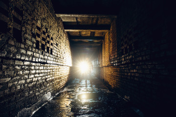 Silhouette of man with flashlight in dark dirty brick underground tunnel or sewerage corridor
