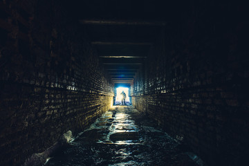 Silhouette of man with flashlight in dark dirty brick underground tunnel or sewerage corridor - obrazy, fototapety, plakaty