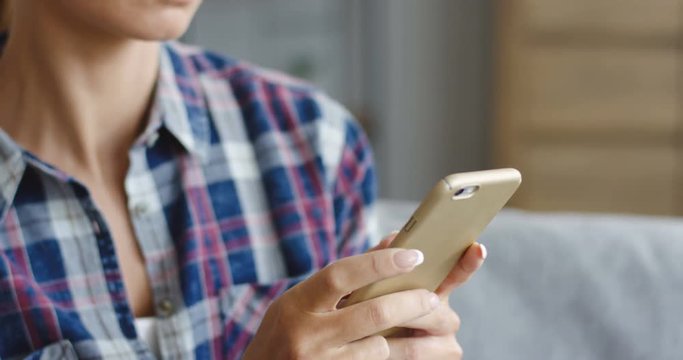Close up of the hands of the blonde woman holding a smartphone and typing on it at home. Inside