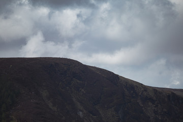 People on the peak of the Spinc ridge overlooking the spectacular Glendalough Valley in Wicklow Natural Park in Ireland. Dramatic clouds. 
