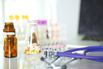 closeup of the desk of a doctors office with a stethoscope in the foreground and a bottle with pills in the background