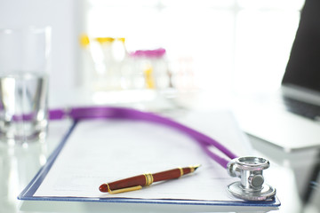 closeup of the desk of a doctors office with a stethoscope in the foreground and a bottle with pills in the background