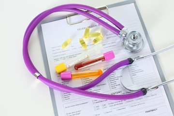 closeup of the desk of a doctors office with a stethoscope in the foreground and a bottle with pills in the background