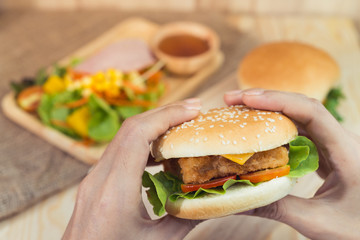Fast food or health concept - Close up of woman hands holding hamburger before eat on table with retro tone.