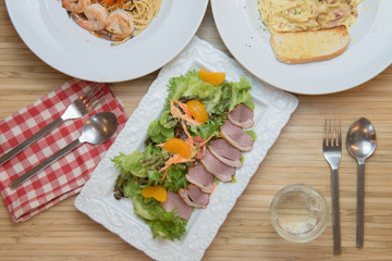 Top view of fresh vegetable salad with duck breast and orange on wood background.