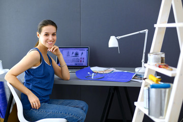 Young woman sitting at the desk with instruments, plan and laptop