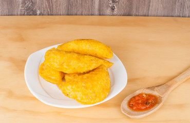 Colombian empanada with spicy sauce on wooden background