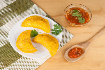 Colombian empanada with spicy sauce on wooden background