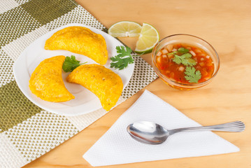 Colombian empanada with spicy sauce on wooden background