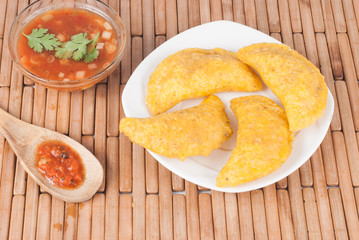 Colombian empanada with spicy sauce on wooden background