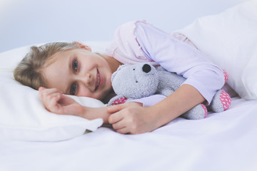 Child little girl sleeps in the bed with a toy teddy bear.