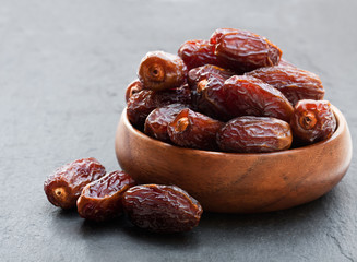 Dried  dates in wooden bowl on black stone background