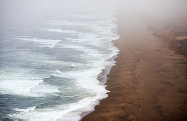 Long empty beach disappears into dense low fog on the northern California coast