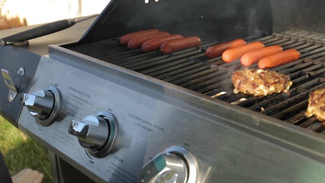 man opening a grill lid to reveal cooking hamburgers and hot dogs
