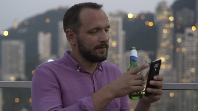 Young man texting on smartphone and drinking beer in skybar 
