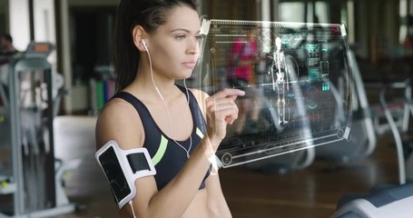 Futuristic portrait of a beautiful girl in the gym on a stationary bike uses a hologram to strengthen her body and heart heartbeat and pressure Concept future of humanity,new technology futuristic gym - Powered by Adobe
