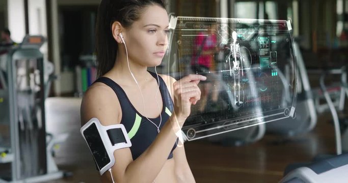 Futuristic portrait of a beautiful girl in the gym on a stationary bike uses a hologram to strengthen her body and heart heartbeat and pressure Concept future of humanity,new technology futuristic gym