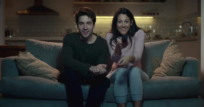 Young couple sitting on a sofa at night  preparing to watch their favourite movie or tv show