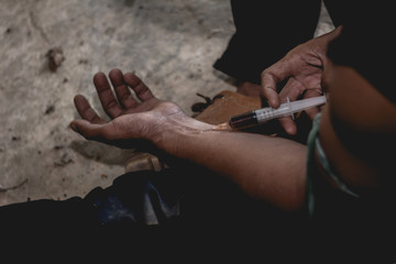 Men hand of a drug addict and a syringe with narcotic syringe sitting on the floor. Anti drug concept.