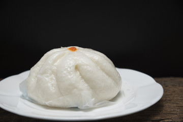 A steamed bun on a white dish and black background