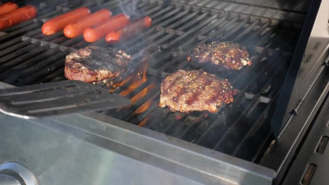 flipping burgers cooking on a grill with some hotd ogs in the back
