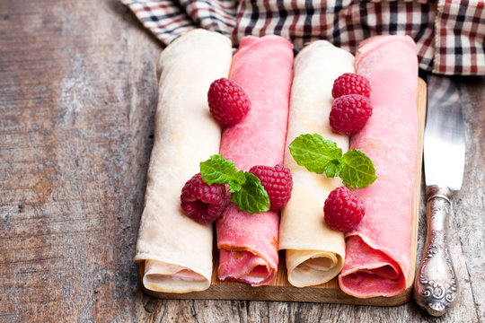 Rolled  milk and raspberry pancakes on wooden table