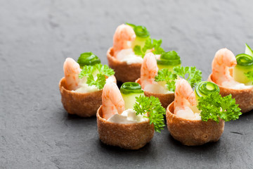 Salted  croustades crispy pastry stuffed with cream cheese and prawns on black stone background