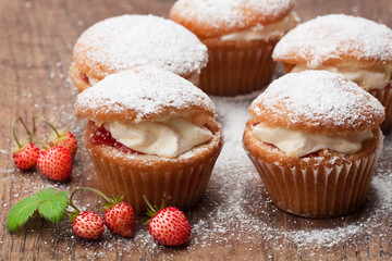 Cupcakes  stuffed with white cream and wild strawberry on wooden table
