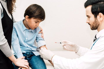 Doctor in protective gloves giving injection with little boy child and mom on doctors table in hospital.healthcare and medicine